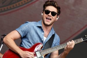 Niall Horan playing electric guitar live on stage with sunglasses and airpods