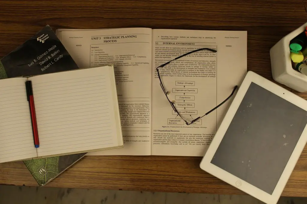 iPad next to notebook and open textbook in article about taking digital notes.