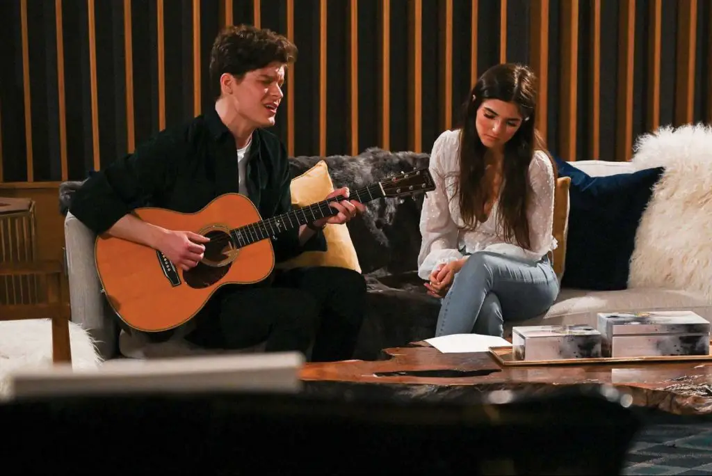 Screenshot from Listen to Your Heart, where a person plays the acoustic guitar for someone else on a couch
