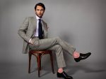 Penn Badgley sitting in a chair in a nice suit
