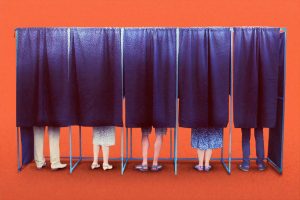 People behind voting booth curtains.