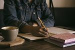 Image of person writing in a notebook on a table, in article about authors building a fan base