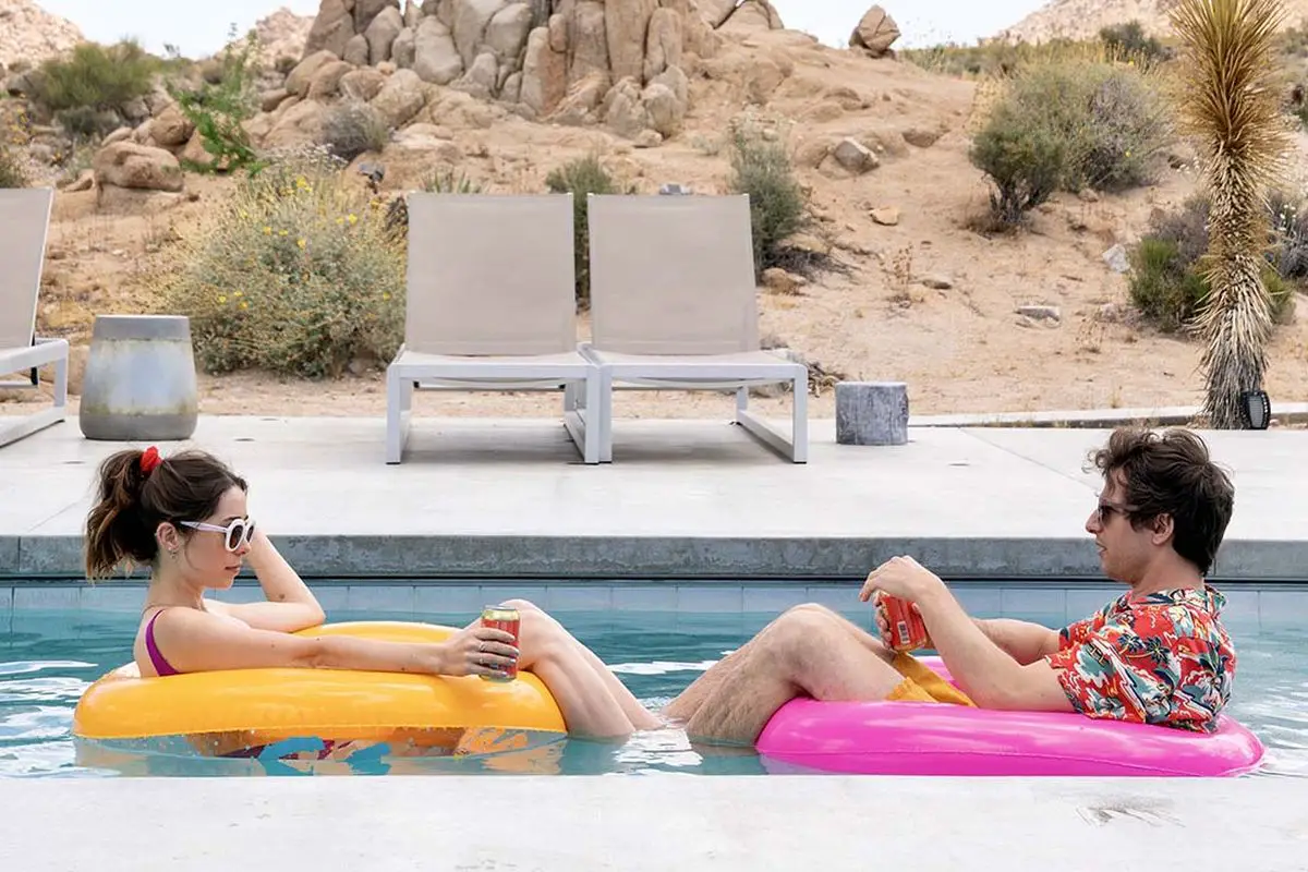 The main characters of Palm Springs float in a pool at their Palm Springs time wrap get away.