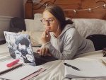 Image of productivity vlogger Hannah Elise studying on a laptop on her bed with notebooks surrounding her