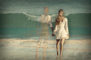 Man and woman hold hands in front of the ocean.