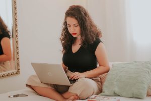 An image of a woman sitting on her bed doing school on a laptop