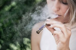 Image of a blonde haired woman smoking weed with smoke billowing around her