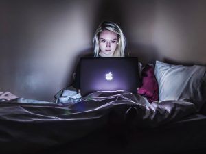 Image of a woman sitting in bed looking at a computer, in an article about fake news.