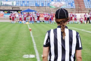 A coach stands on the football field observing her team.