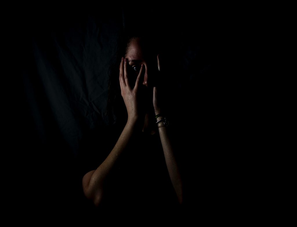 Image of a woman shrouded in darkness covering her face, in an article about imposter syndrome.