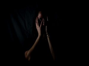 Image of a woman shrouded in darkness covering her face, in an article about imposter syndrome.