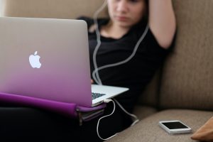 For an article about Skillshare versus LinkedIn Learning, an image of a person with earbuds in, on the couch, looking at their laptop