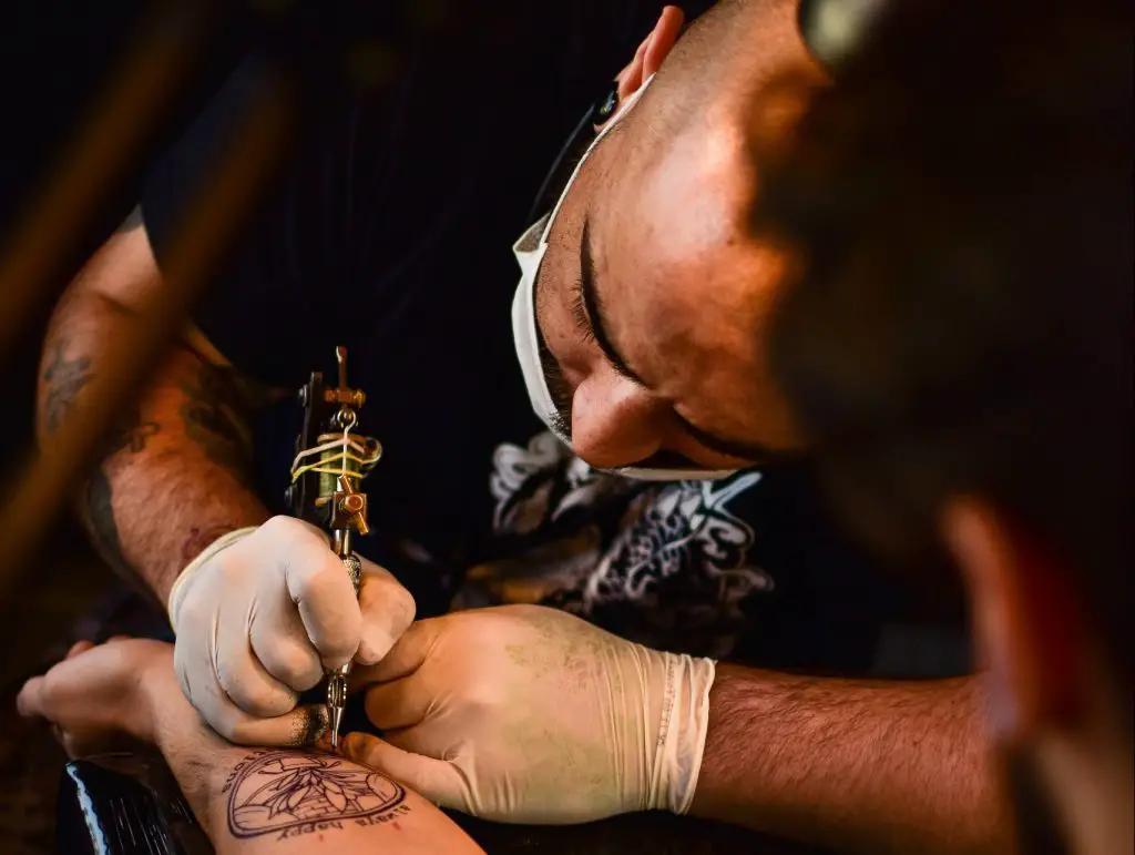 Image of a man giving tattoos while wearing a mask