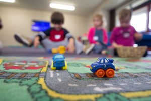 a photograph of three children in the foster care system playing with toy cars