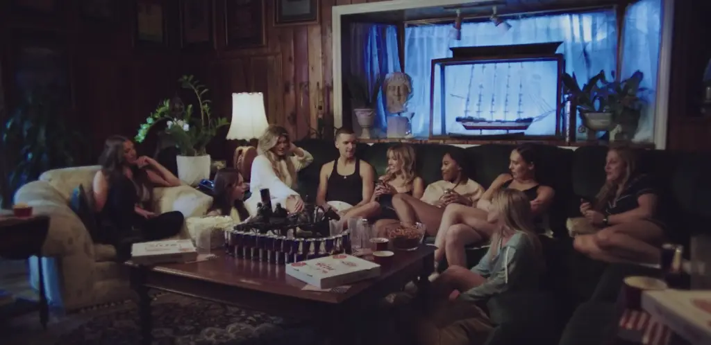 Olivia O'Brien and a group of friends sitting together in a living room setting for a music video from her album Episodes: Season 1. (Image via Google Images)