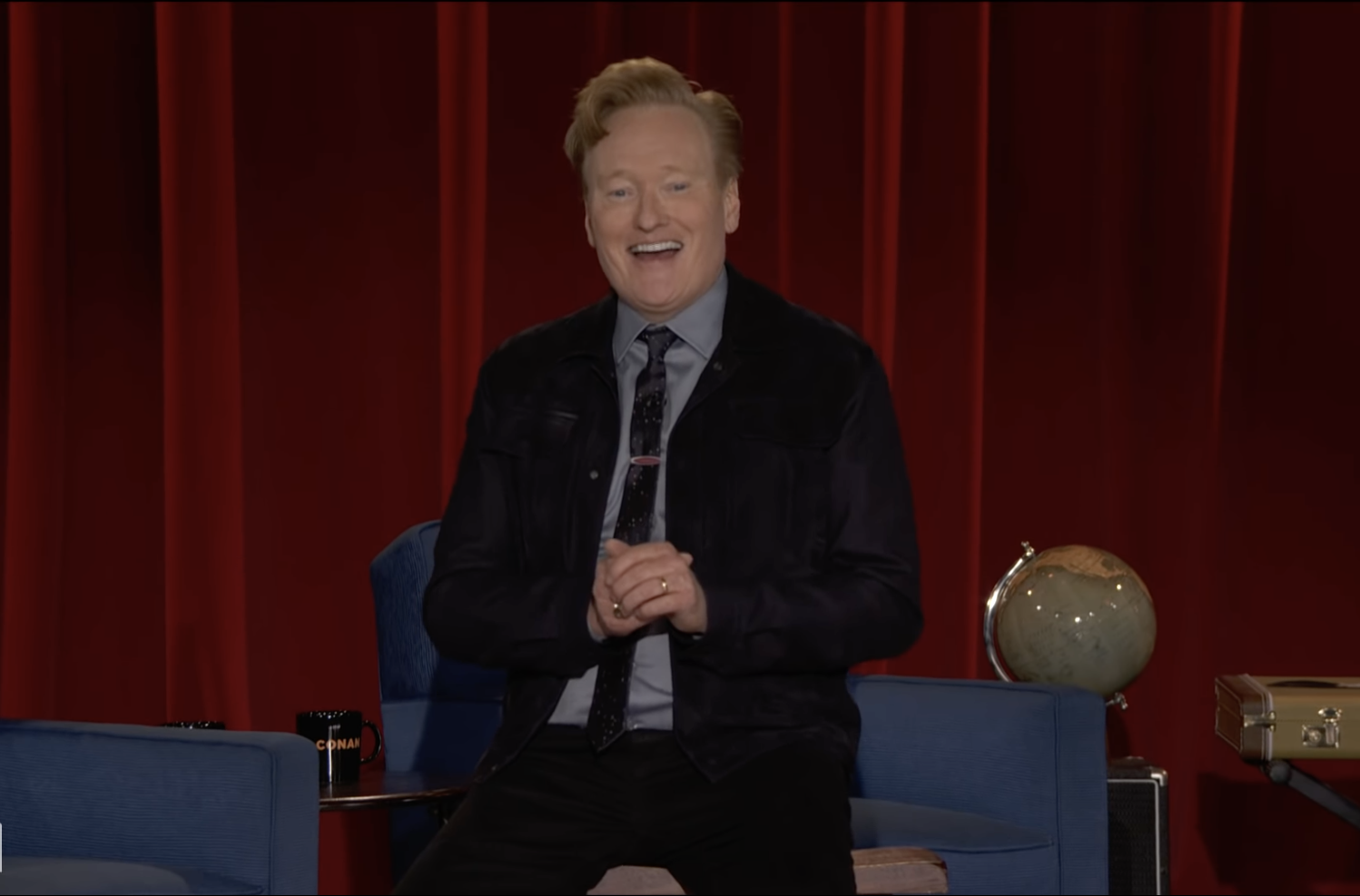 A picture of comedian Conan O'Brien against a dark red curtain.