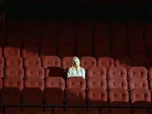 In an article about her album Happier Than Ever, Billie Eilish sits alone in an empty theater filled with red chairs.