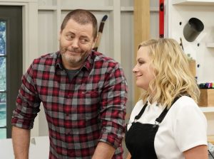 In a show about "Making It," actors Nick Offerman and Amy Poehler stand beside each other in a warehouse.