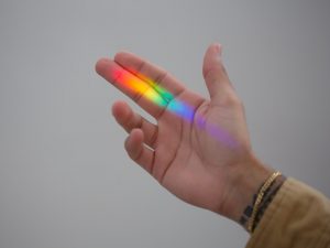 A picture of a hand with a rainbow light leaking onto his fingers.