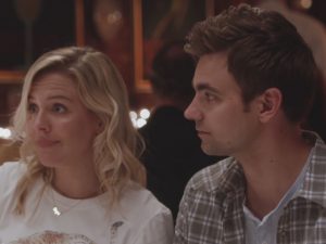 In an article about series the Other Two, a man and a woman sit at a restaurant table next to each other.