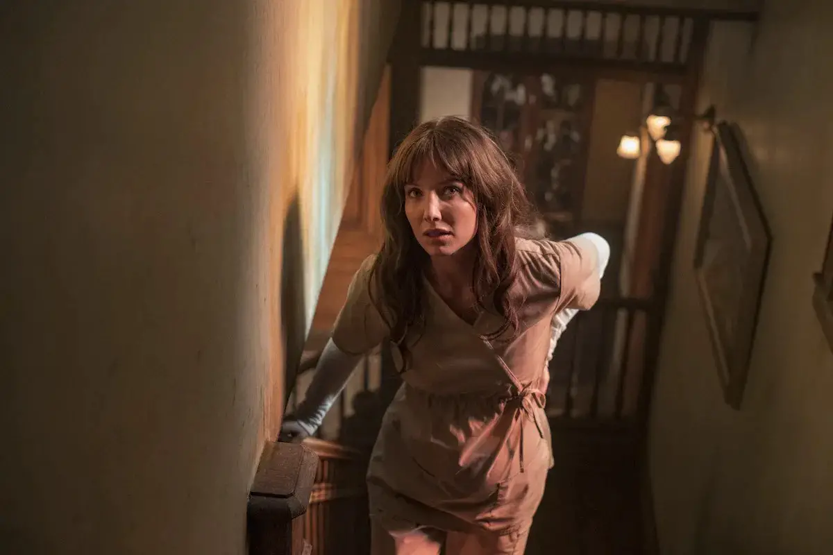 A woman from the film Malignant worriedly walks up stairs while holding her back.