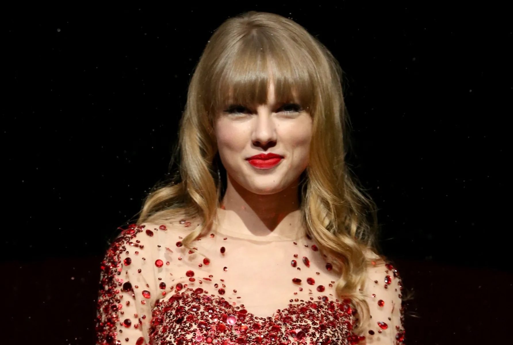 Taylor Swift smiling against a black background.
