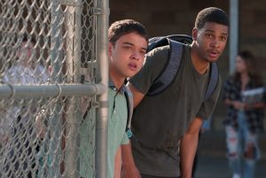 Two characters from Netflix's On My Block peek around a fence.