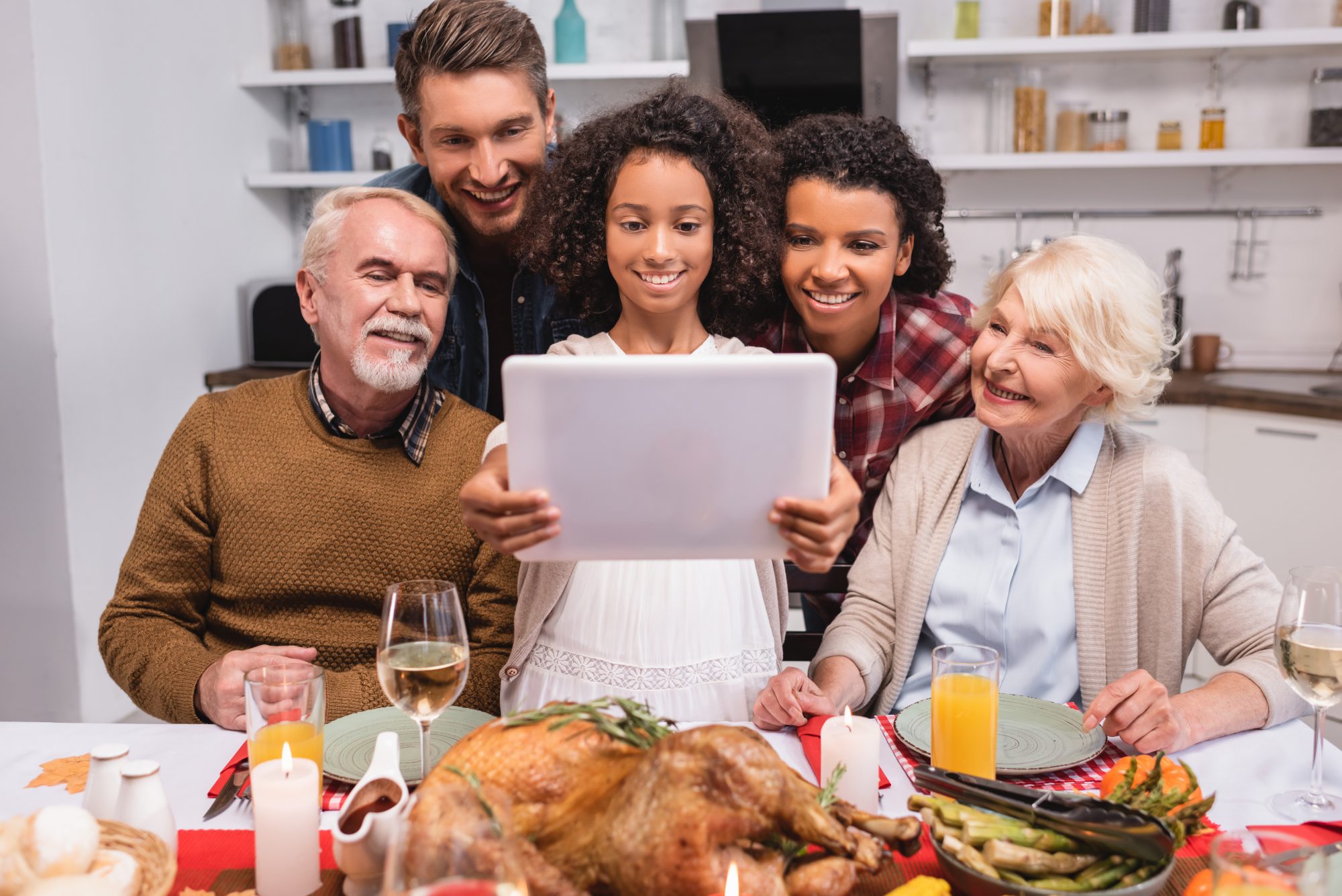 A family surrounds a computer with Thanksgiving dinner on the table for Zoom Thanksgiving.