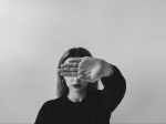 Gray-scale photo of a woman holding her hand in front of her eyes for an article about self-confidence.