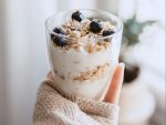 A photo of a hand holding a cup of yogurt, granola and blueberries for an article about healthy eating in college.