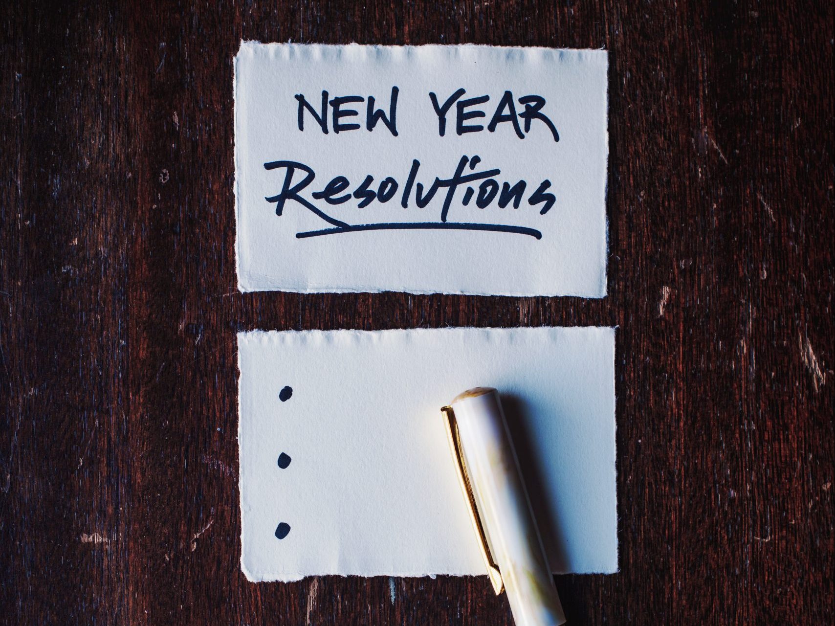 Photo of a piece of lined paper with "New Year's Resolutions" written at the top and a pen beside it.