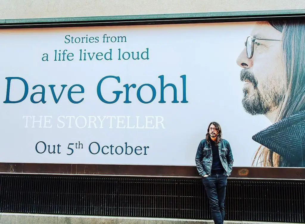 Dave Grohl standing in front of ad for memoir The Storyteller