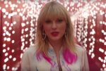 Taylor Swift singing in front of strands of pink lights in her video for her song Lover.