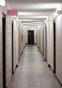 Image facing down a starkly white corridor of closed doors.