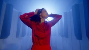 Music artist Mitski looking away from the camera in a red satin outfit.