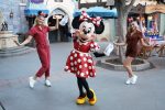 Minnie Mouse flanked by two Disney park employees