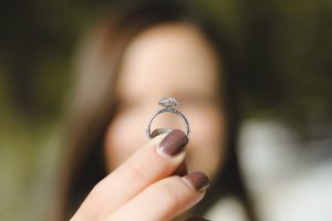 Woman blurred in background as she holds up her wedding ring to symbolize love is blind.