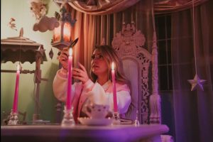 Scene Queen sitting at a table lighting candles in her video for Pink Rover