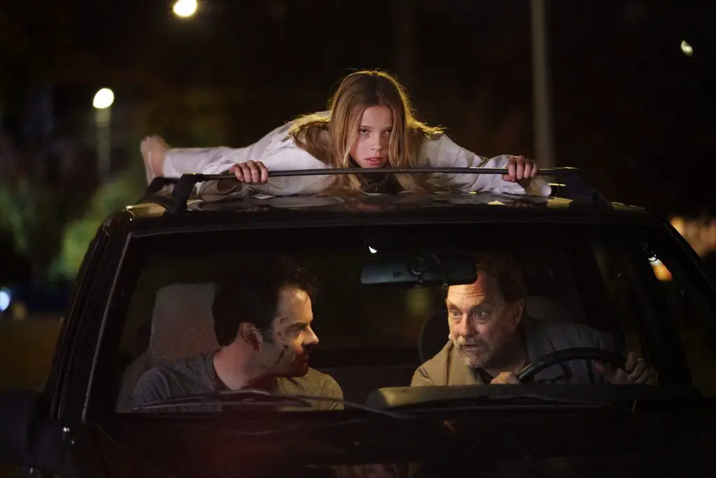 A screenshot of Barry shows two men in a car with a girl on the roof.