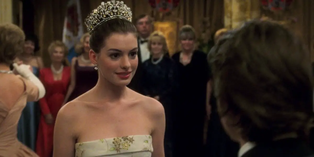 In an article about Anne Hathaway's Fairy-Tale Films, a screenshot of Anne Hathaway in the Princess Diaries dressed in royal clothing at a ball