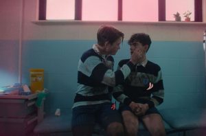 Two boys sitting in a locker room, comforting each other.