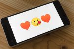 in an article about datings apps and queer women, a phone whose screen has two heart emojis with a kissy face emoji in between them
