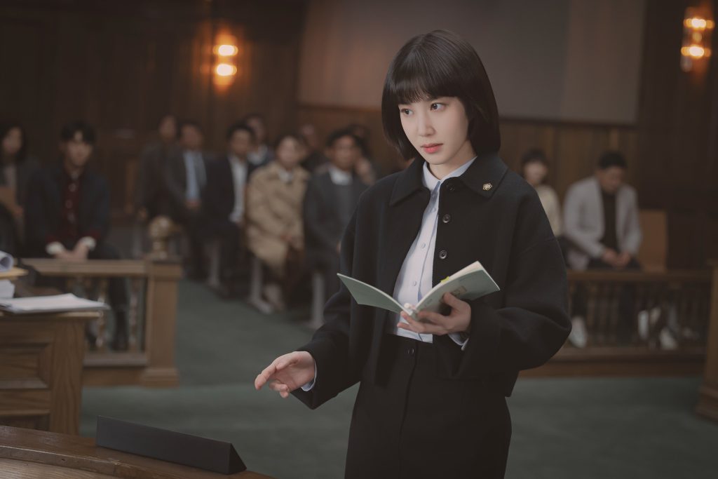 An image of Extraordinary Attorney Woo shows the title character standing in a court room with a book.