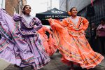 in article about hispanic heritage month, two women in purple and orange dresses dancing in the street