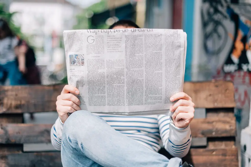 a picture of someone reading local news shows a person sitting on a bench with a newspaper