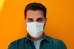 In an article about the flu outbreak, a person wearing a medical mask stands in front of an orange wall.