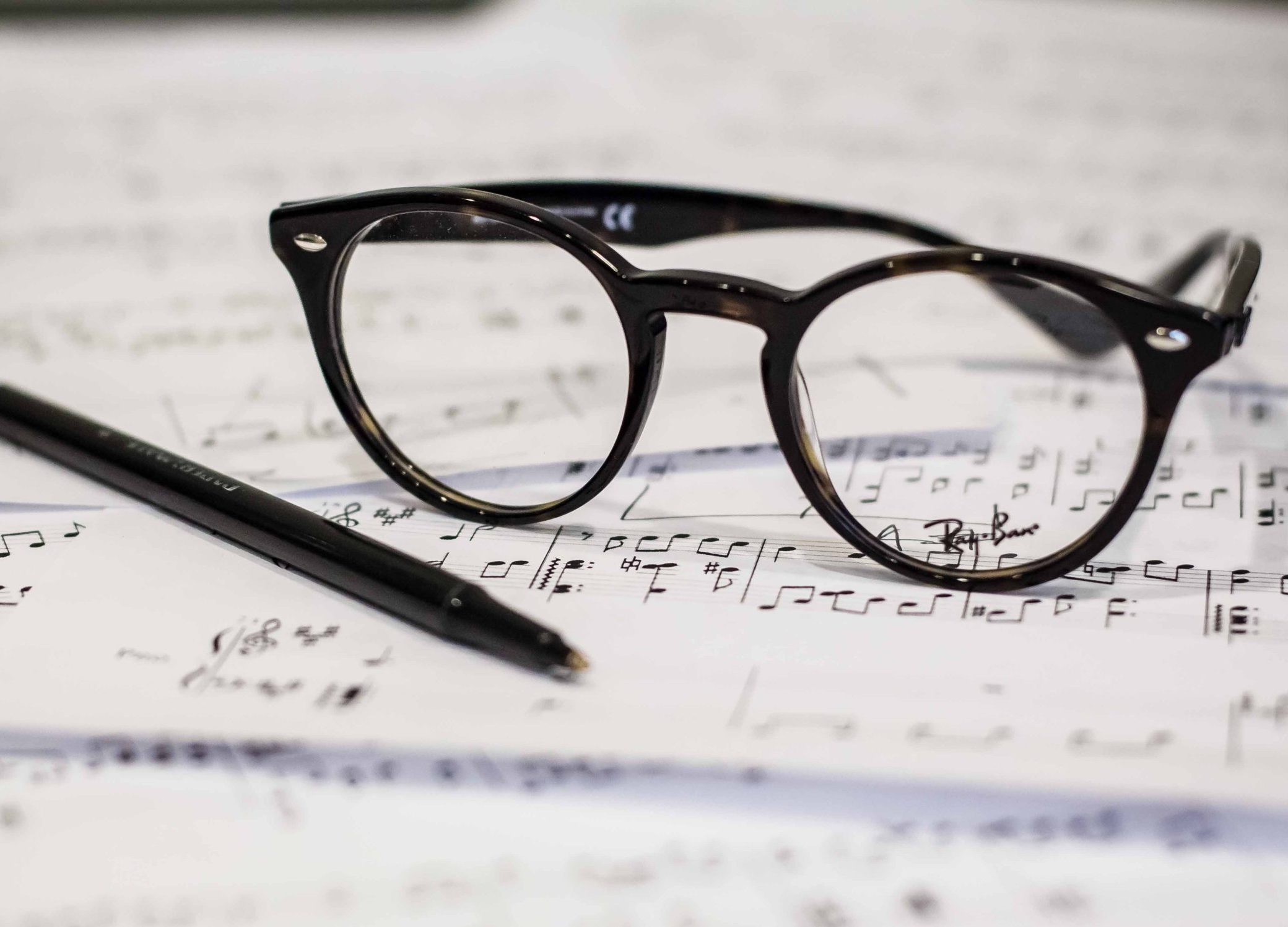 In an article about classical music, a pile of sheet music with a pair of black glasses and a pen on top.