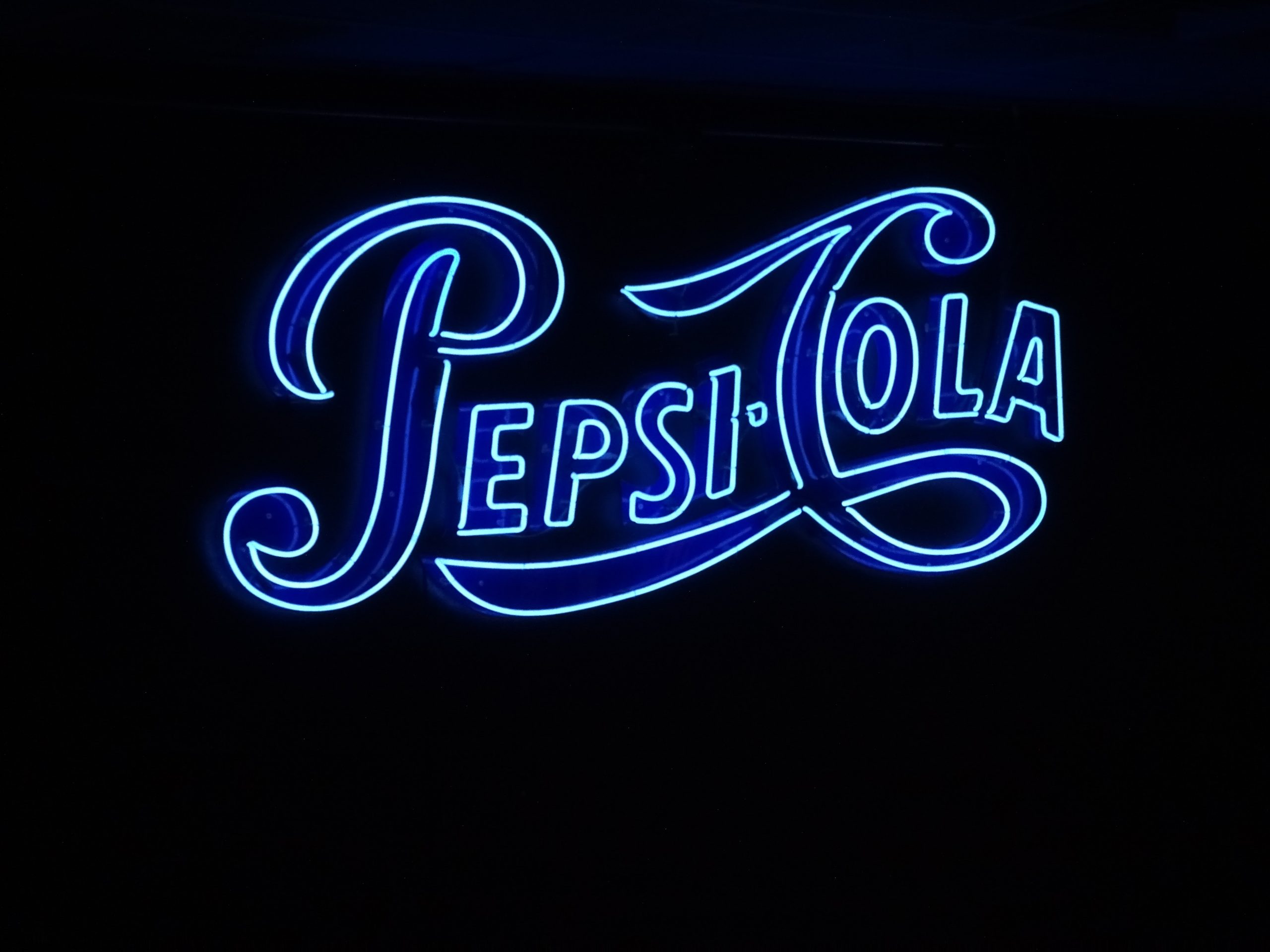 In an article about the Pepsi company, a blue neon sign reads 'Pepsi-Cola.'
