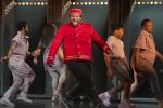 In an article about musicals, a theatre usher in a red uniform does a jazz square in front dancers in muted colors during the 2022 Tony Award performance for the musical 'A Strange Loop.'