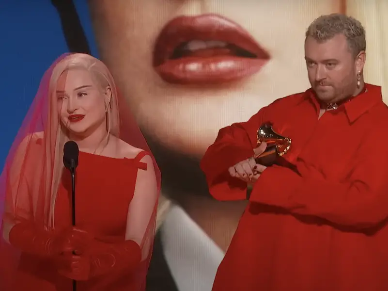 Kim Petras and Sam Smith in red outfits accepting their award for "Unholy" at the Grammy Awards.